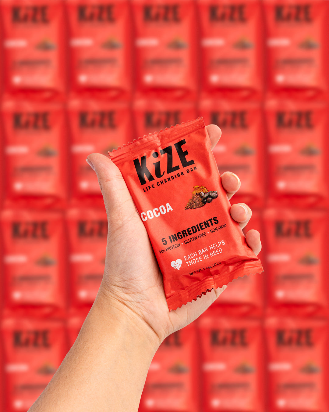 Hand holding KiZE cocoa life changing bar with blurred background of product boxes