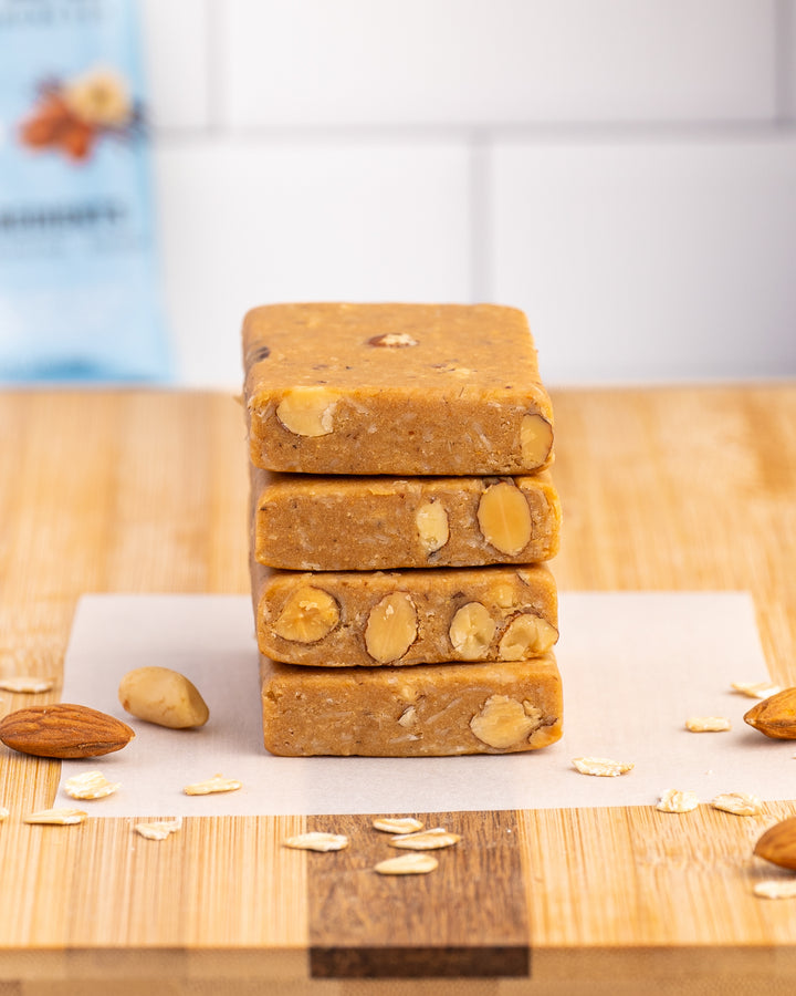 Stack of almond protein bars on wooden surface with scattered almonds and oats